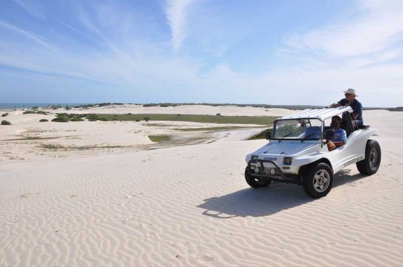 Passeio de buggy amarelo nas dunas, com mato seco e céu azul ao fundo.